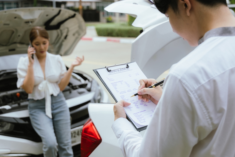 A young Caucasian man and an Asian woman inspect a damaged car after an auto accident